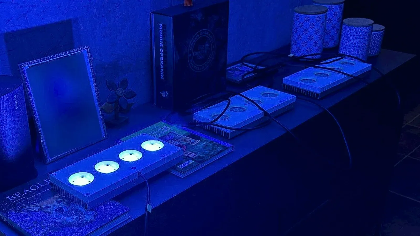 Die drei gereinigten Hydra 64HD liegen zum Test verkabelt auf der Kommode im Wohnzimmer. Die vorderste leuchtet mit ihren vier LED-Modulen blau, die beiden dahinter sind ausgeschaltet.
